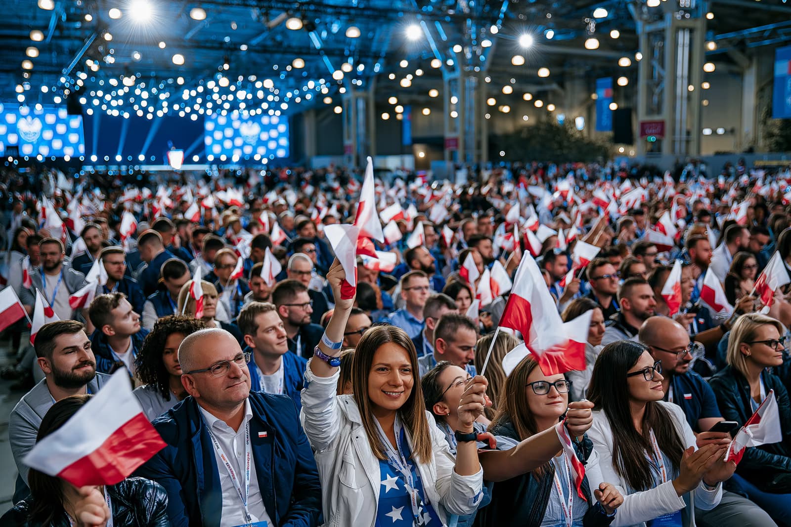 Eine vollbesetzte Messehalle mit vielen Menschen, die unter greller Veranstaltungsbeleuchtung bei der Wahlkampfauftaktveranstaltung der AfD in Magdeburg mit kleinen Fahnen winken; im Hintergrund ist eine Bühne zu sehen.