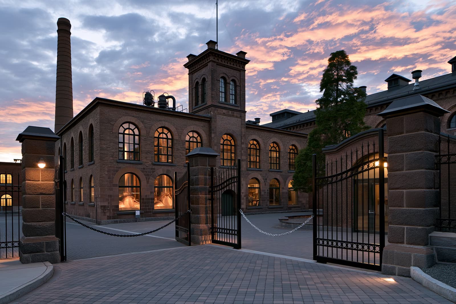 Hinter verschlossenen Toren steht bei Sonnenuntergang ein historisches Brauereigebäude, in dem durch Bogenfenster Kupferkessel zu sehen sind - ein Zeichen für das Ende der Brauerei Eichbaum.