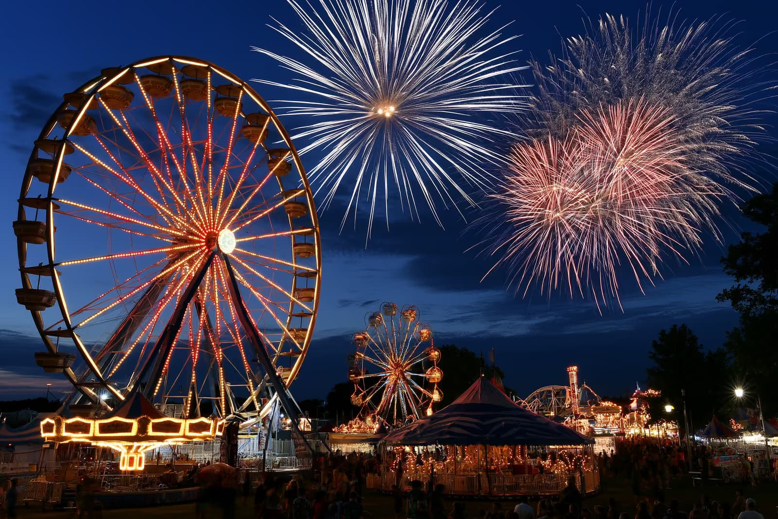 Ein hell erleuchteter Jahrmarkt mit großem Riesenrad und Fahrgeschäften in der Abenddämmerung auf dem Heiligengeistfeld in Hamburg
