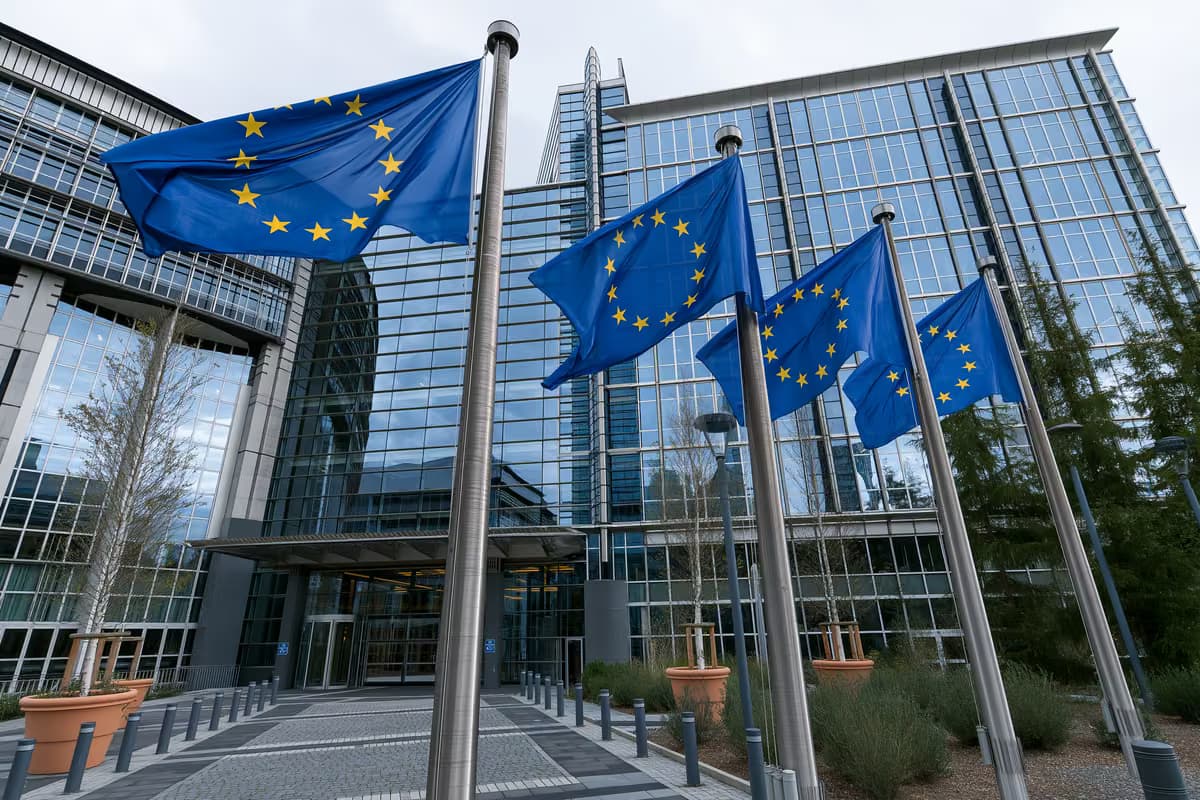 Flaggen der Europäischen Union wehen an Fahnenmasten vor einem modernen Glasgebäude.