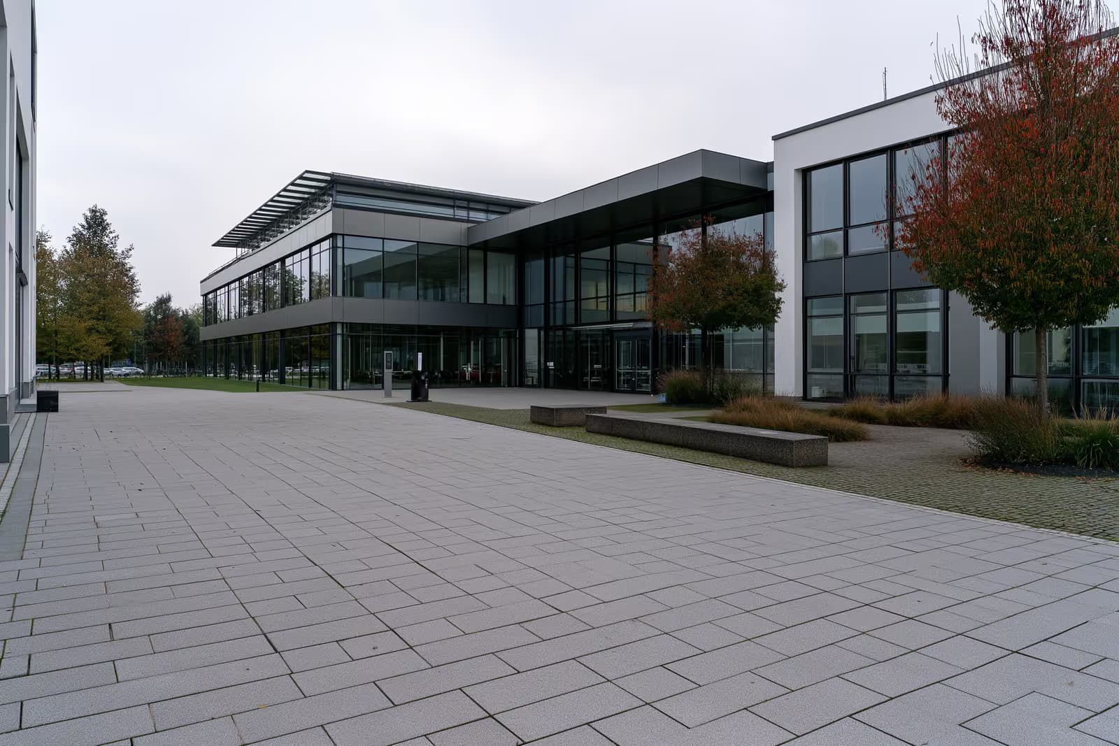 Ein modernes deutsches Arbeitsvermittlungsgebäude mit einem breiten, leeren gepflasterten Vorplatz unter bedecktem Himmel.
