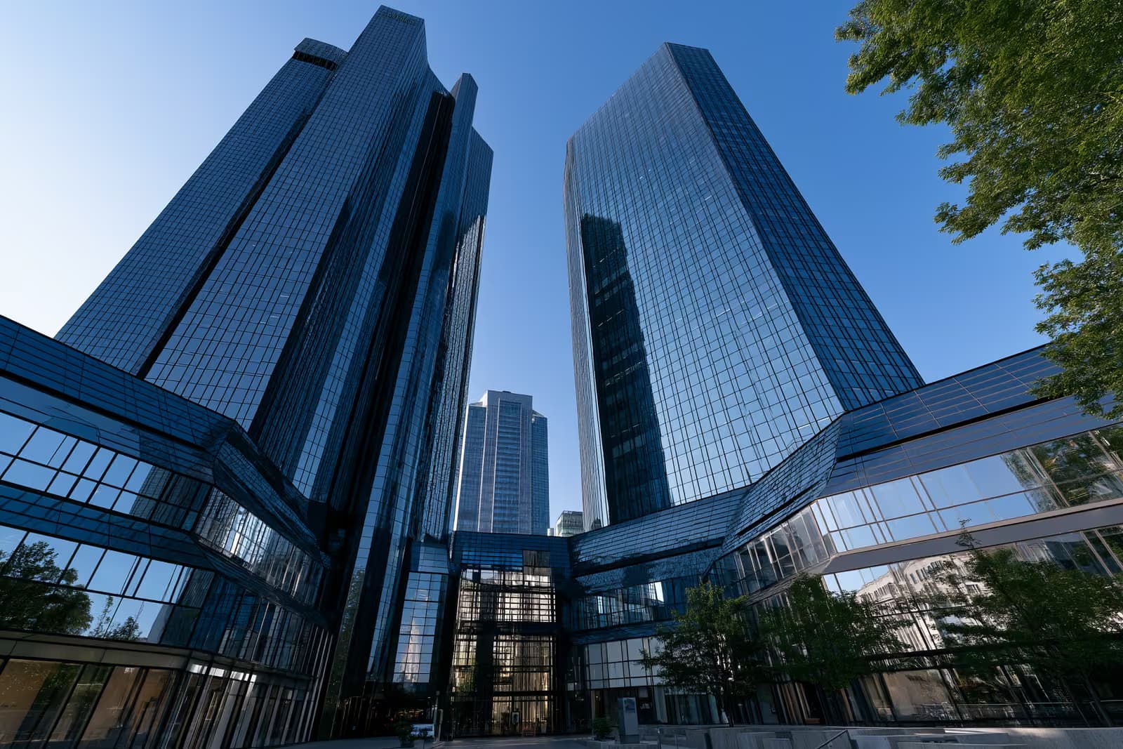 Die beiden gläsernen Banktürme in Frankfurt, die vor einem strahlend blauen Himmel glänzen, von unten gesehen.