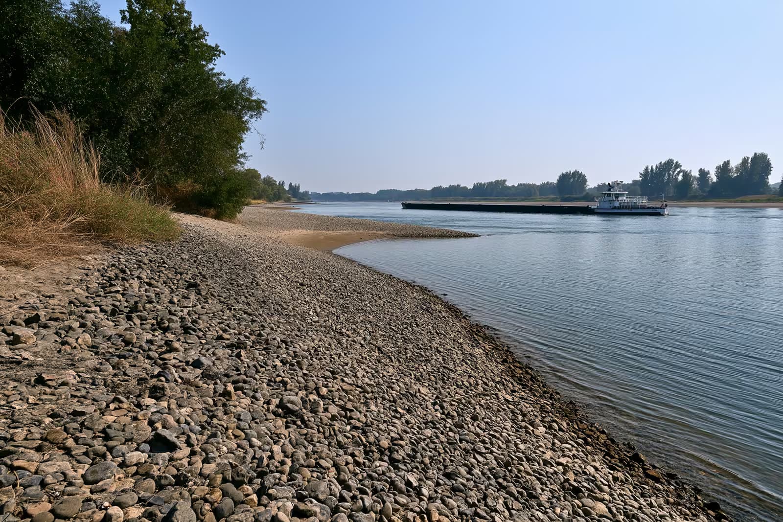 Ein Frachtkahn liegt tief und leicht beladen auf dem schmalen Rheinufer mit freiliegenden Sandbänken.